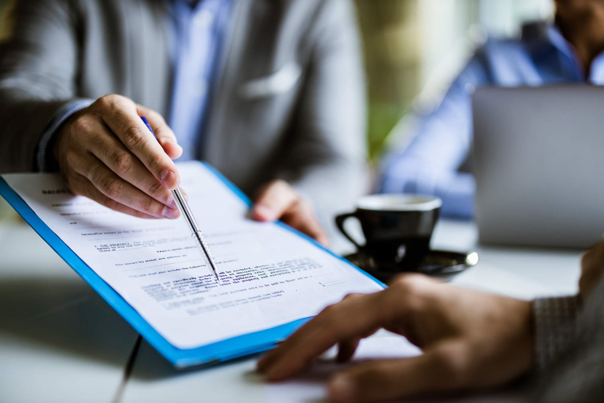 A business professional points to a document as he talks to another man.