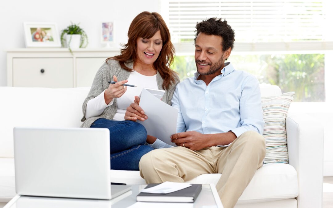 Man and woman sitting together on sofa calculating monthly expenses