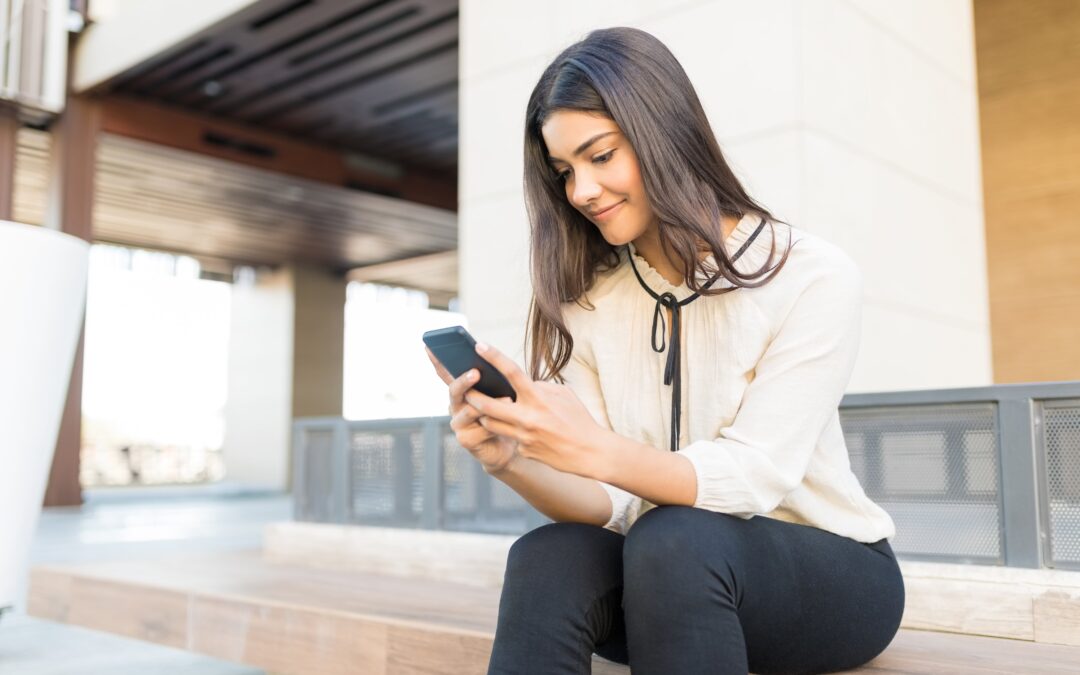 Young woman sitting on office building bench looking at her mobile phone.