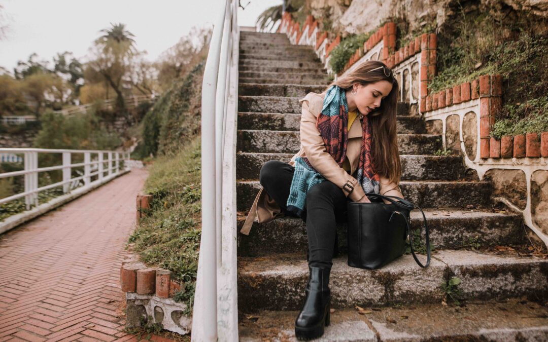 A young woman looking for something in her handbag as she sits on outside stairs.