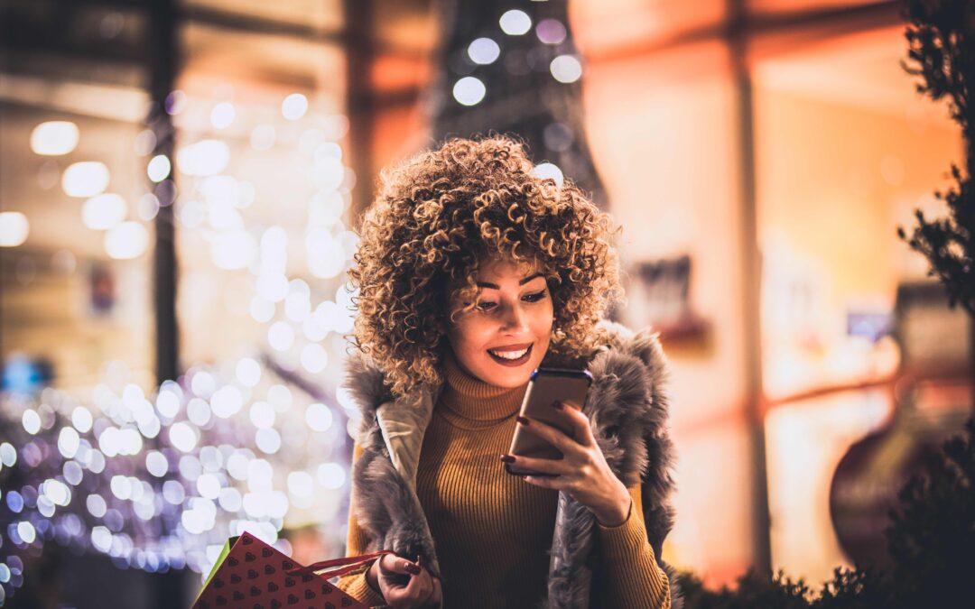 Woman using smartphone and holding shopping bag while standing on the mall background.