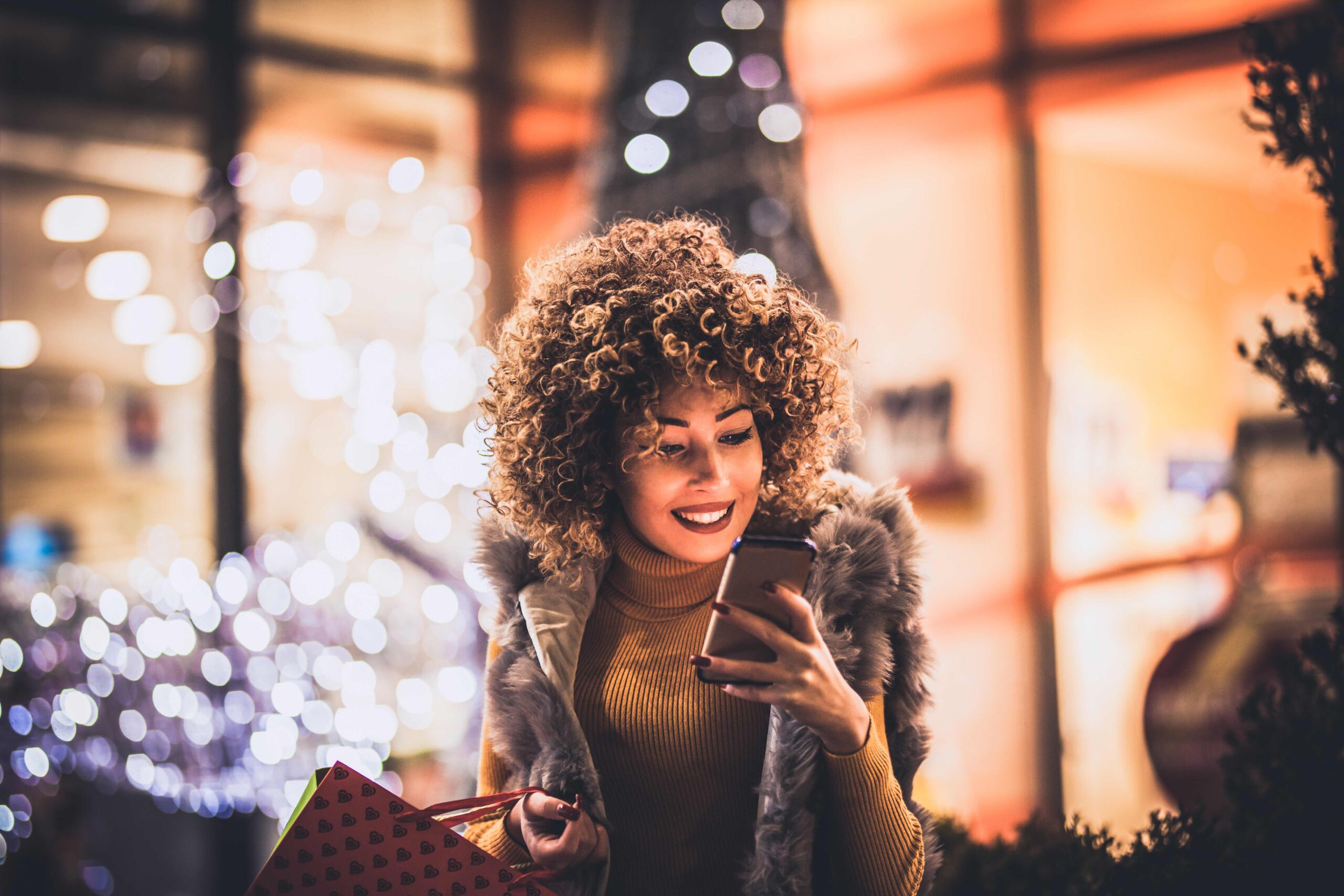 Woman using smartphone and holding shopping bag while standing on the mall background.