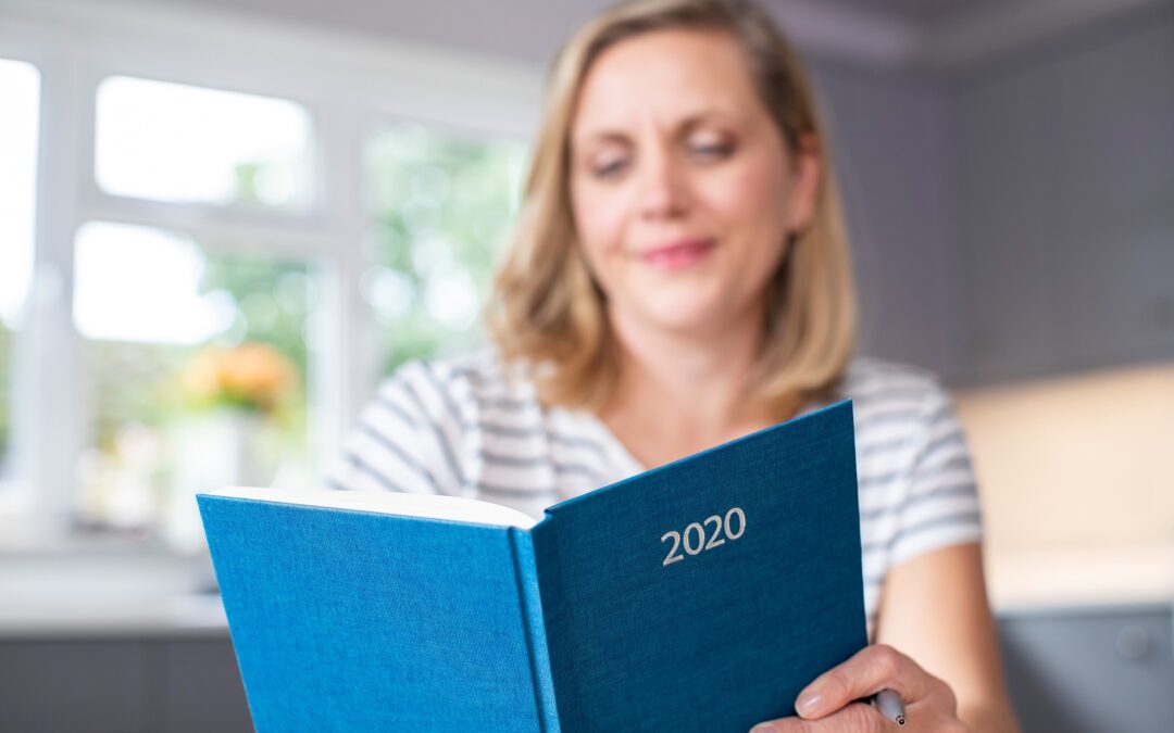 Woman reading resolutions in a bound journal with 2020 written on the cover.