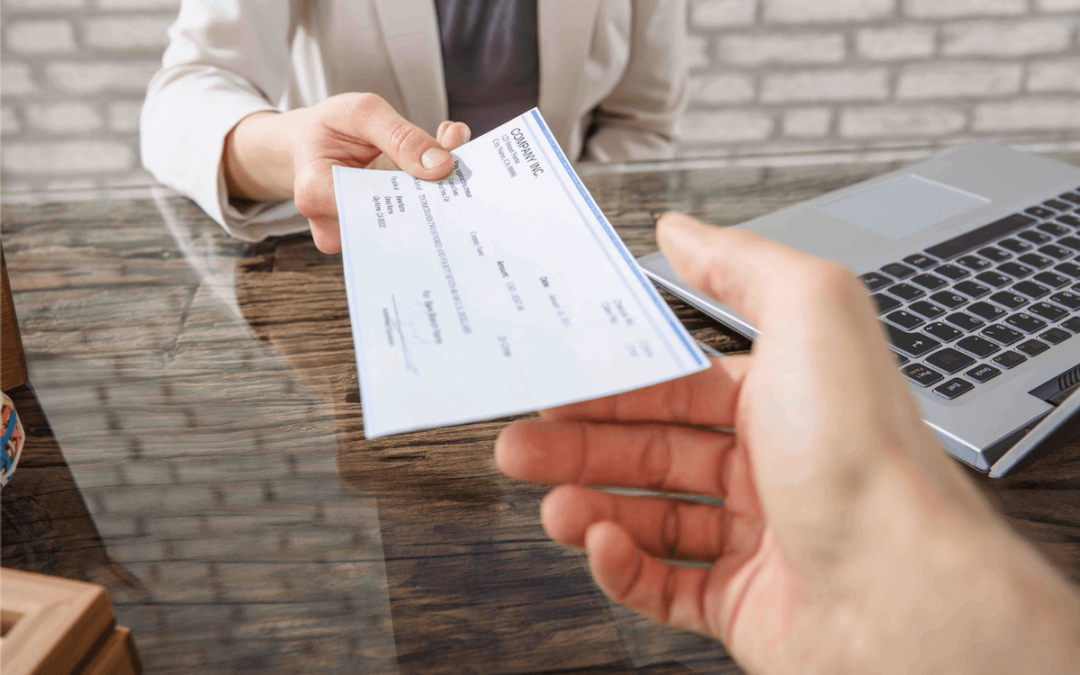 Man's outreached hand is accepting a check from a woman across the desk in a business suit.