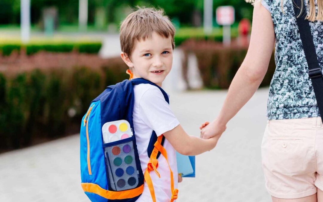 Young boy walking & wearing a backpack as a woman holds his hand.