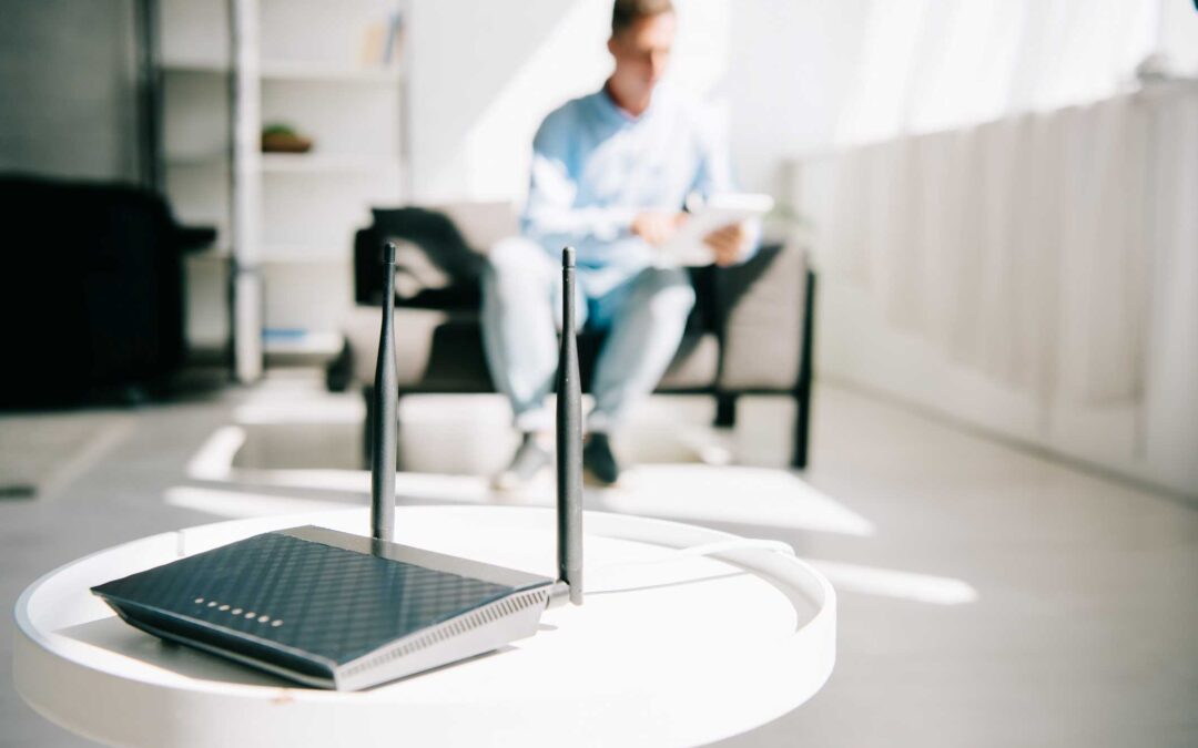 Home Wi-Fi modem on a small, white, round table. A man is using a tablet computer in the background.