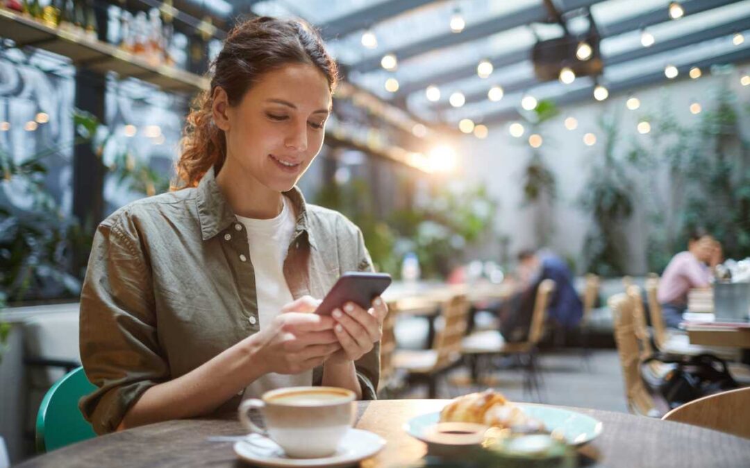 A woman typing on her mobile phone as she sits in a cafe.