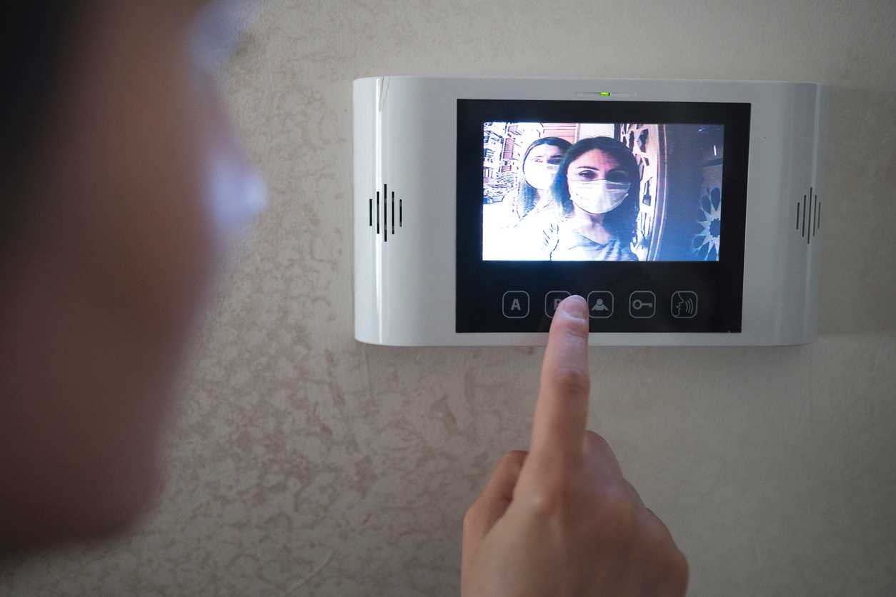 Person looking at doorbell camera video screen. Two women in white face masks are on the screen.