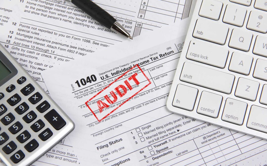 Blank 1040 U.S. tax form with Audit stamped in red. An ink pen, calculator and computer keyboard are also on the table.