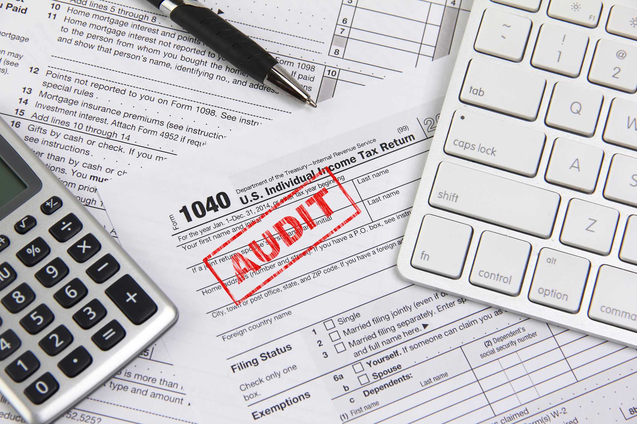 Blank 1040 U.S. tax form with Audit stamped in red. An ink pen, calculator and computer keyboard are also on the table.