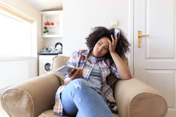 Woman upset about a travel scam while sitting in a chair holding her phone and credit card.