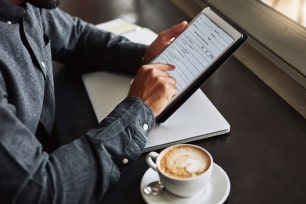 A man is looking at data on a tablet computer. A cup of coffee sits nearby.