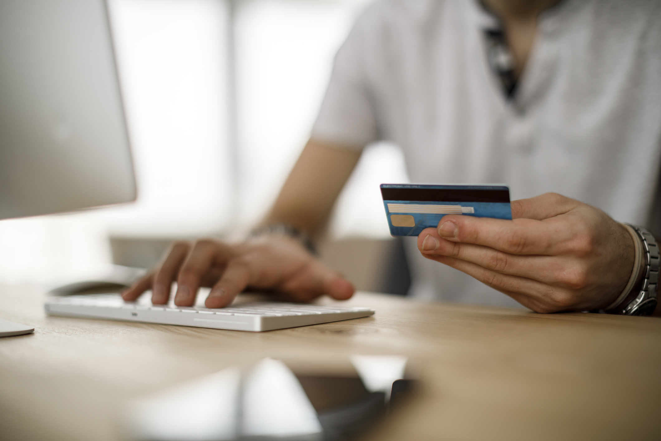 A man holding a credit card is entering information on a keyboard to make an online payment.