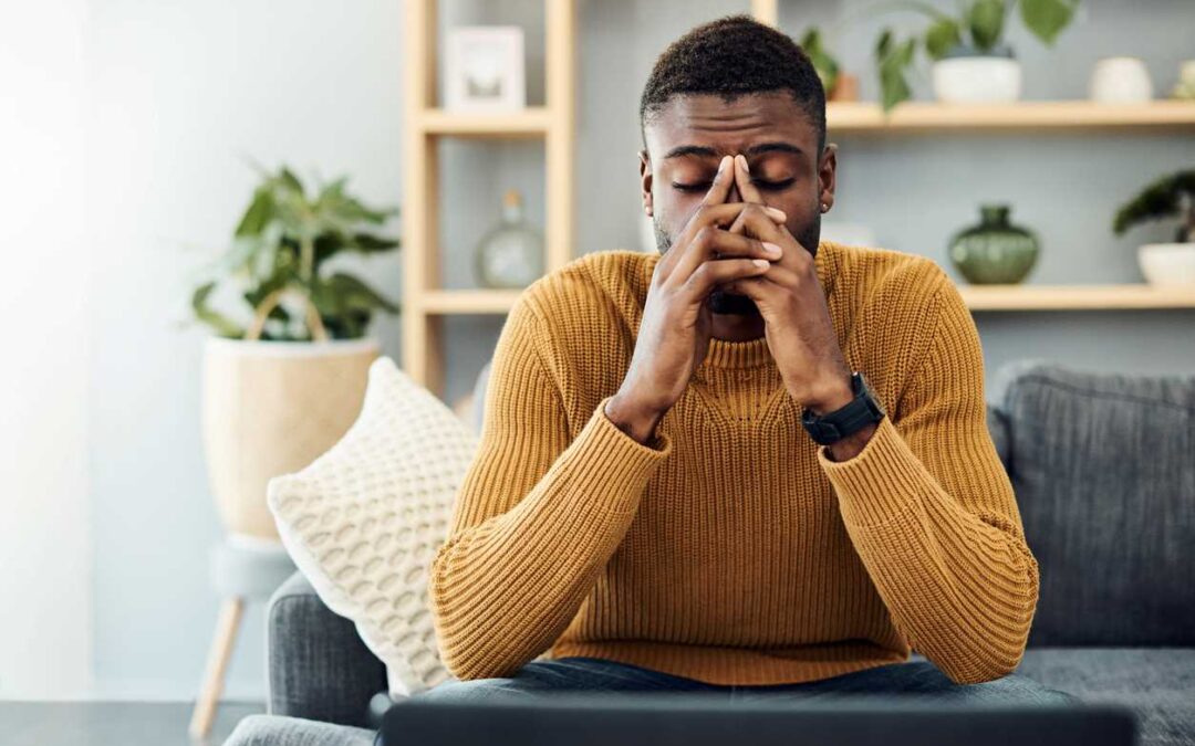 A worried looking unemployed man sitting on a living room couch.