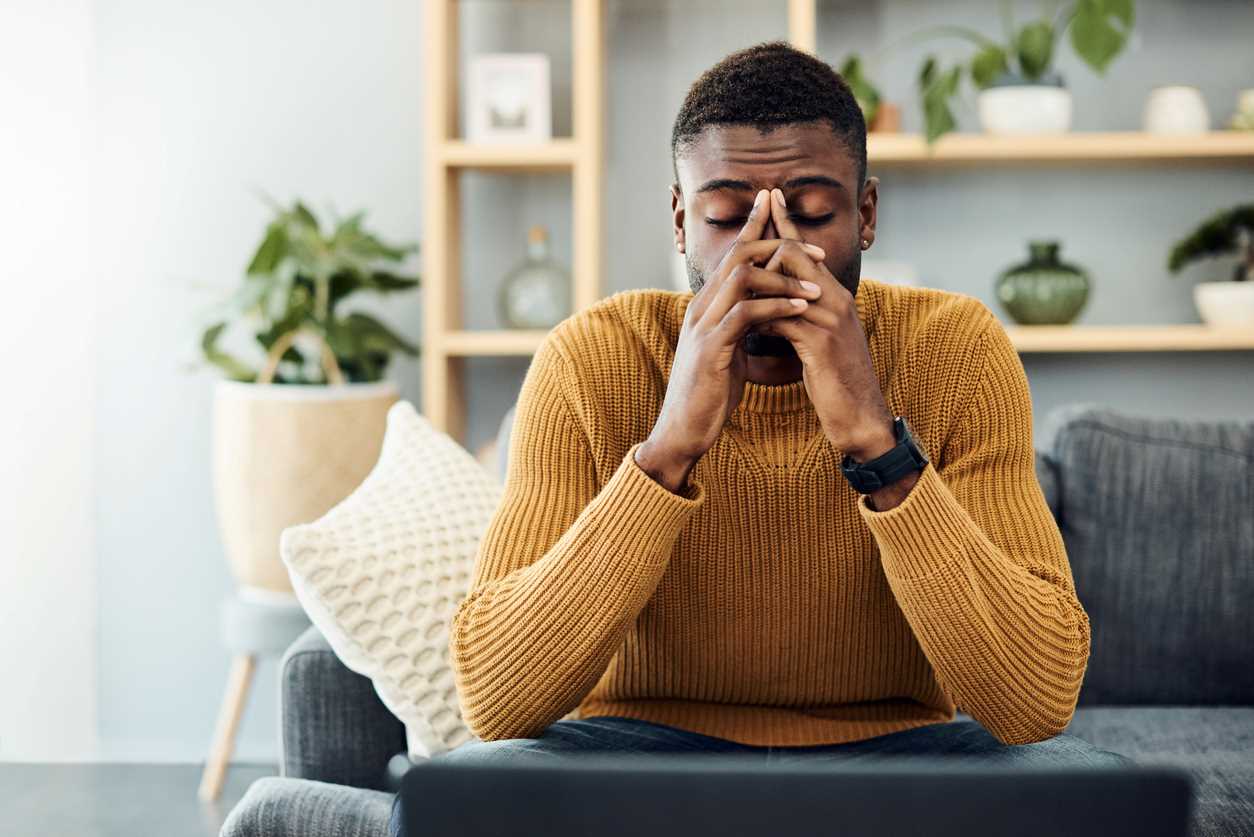 A worried looking unemployed man sitting on a living room couch.