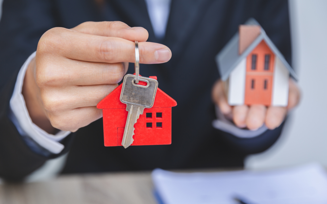 Businessman shown holding house keys and a replica of a small house..