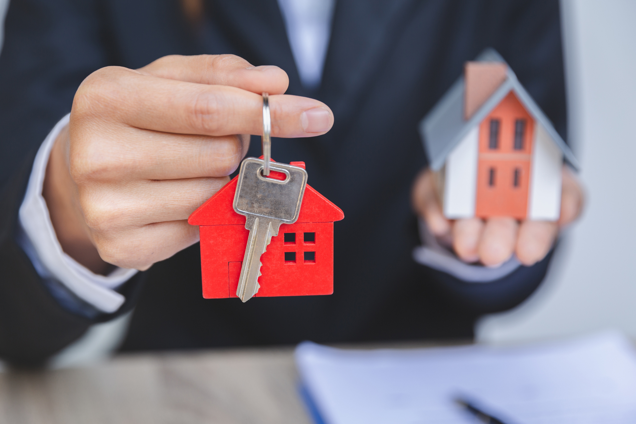 Businessman shown holding house keys and a replica of a small house..