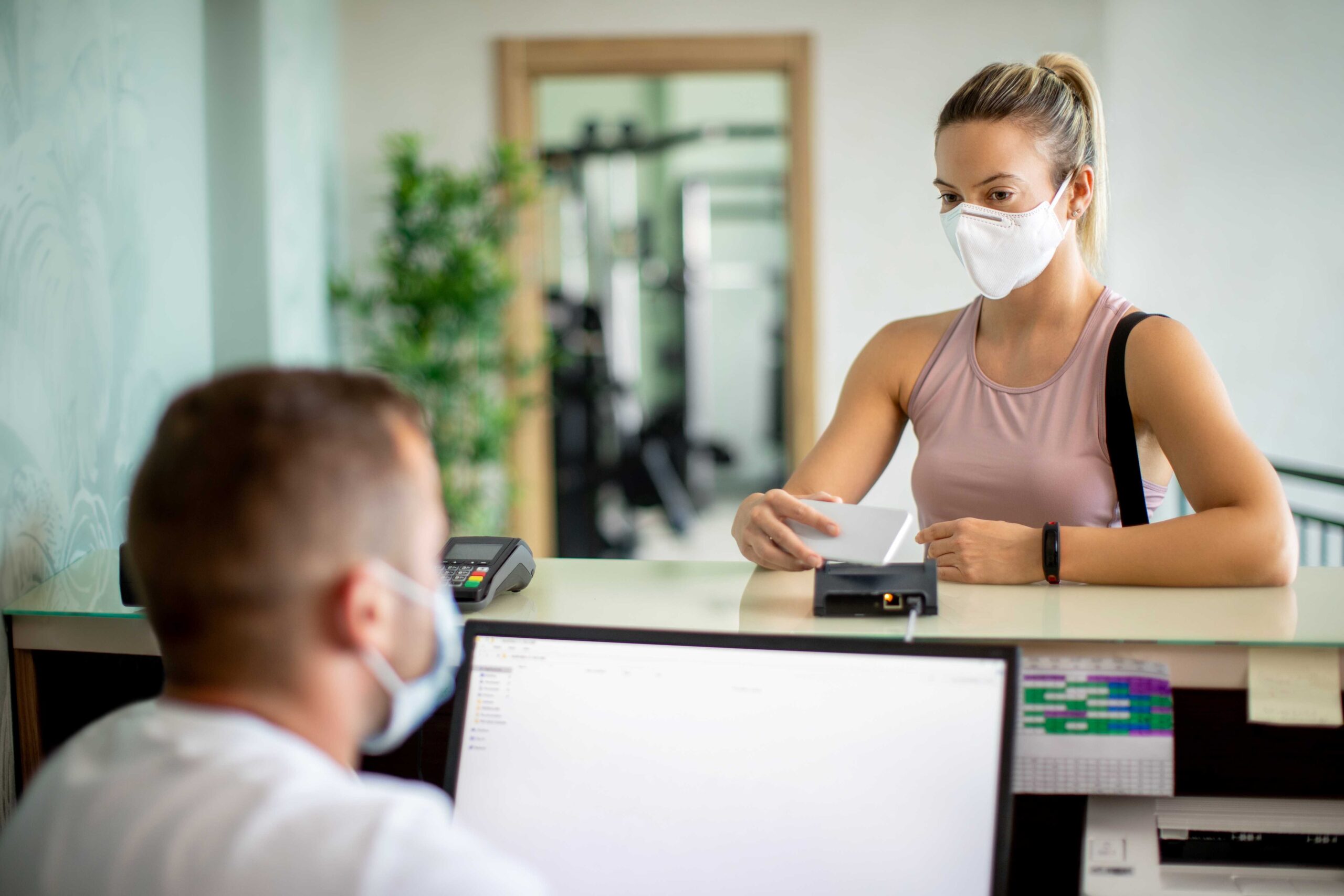 A woman wearing a white mask pays a bill at the gym using a mobile phone scanner.