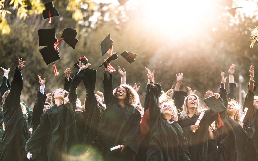 A large group of women wearing black commencement robes and throwing mortar boards in the air to celebrate their graduation.