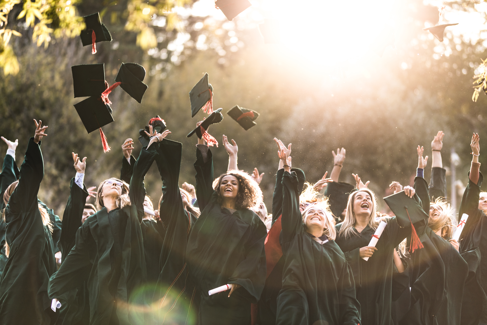 A large group of women wearing black commencement robes and throwing mortar boards in the air to celebrate their graduation.