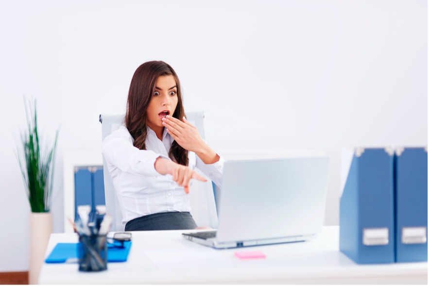 Professional women showing shock as she looks at a contact's reputation information on a laptop while sitting at her work office desk.