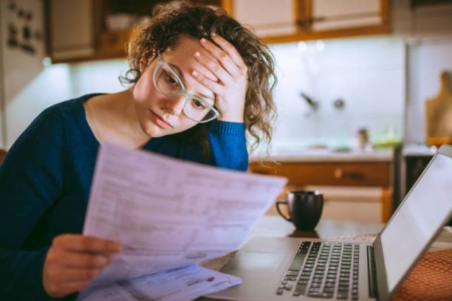 Woman looking worried as she reviews paper work while seated in her kitchen.