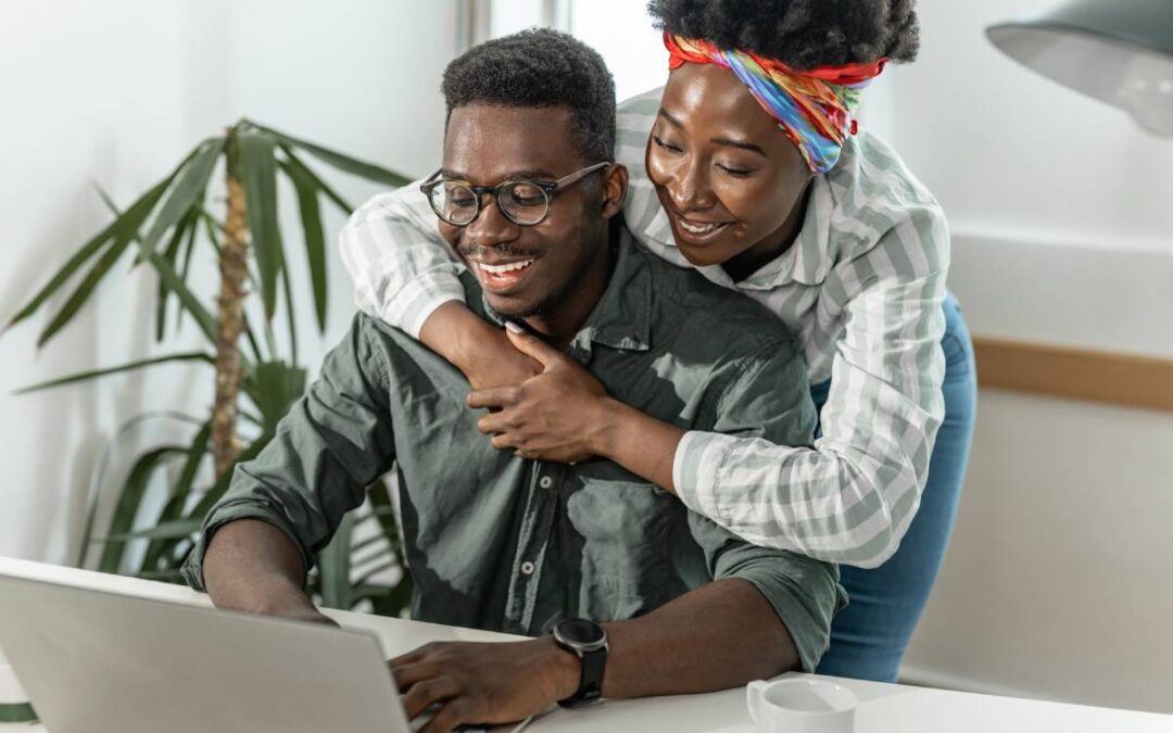 Smiling couple looking at information on a laptop screen.