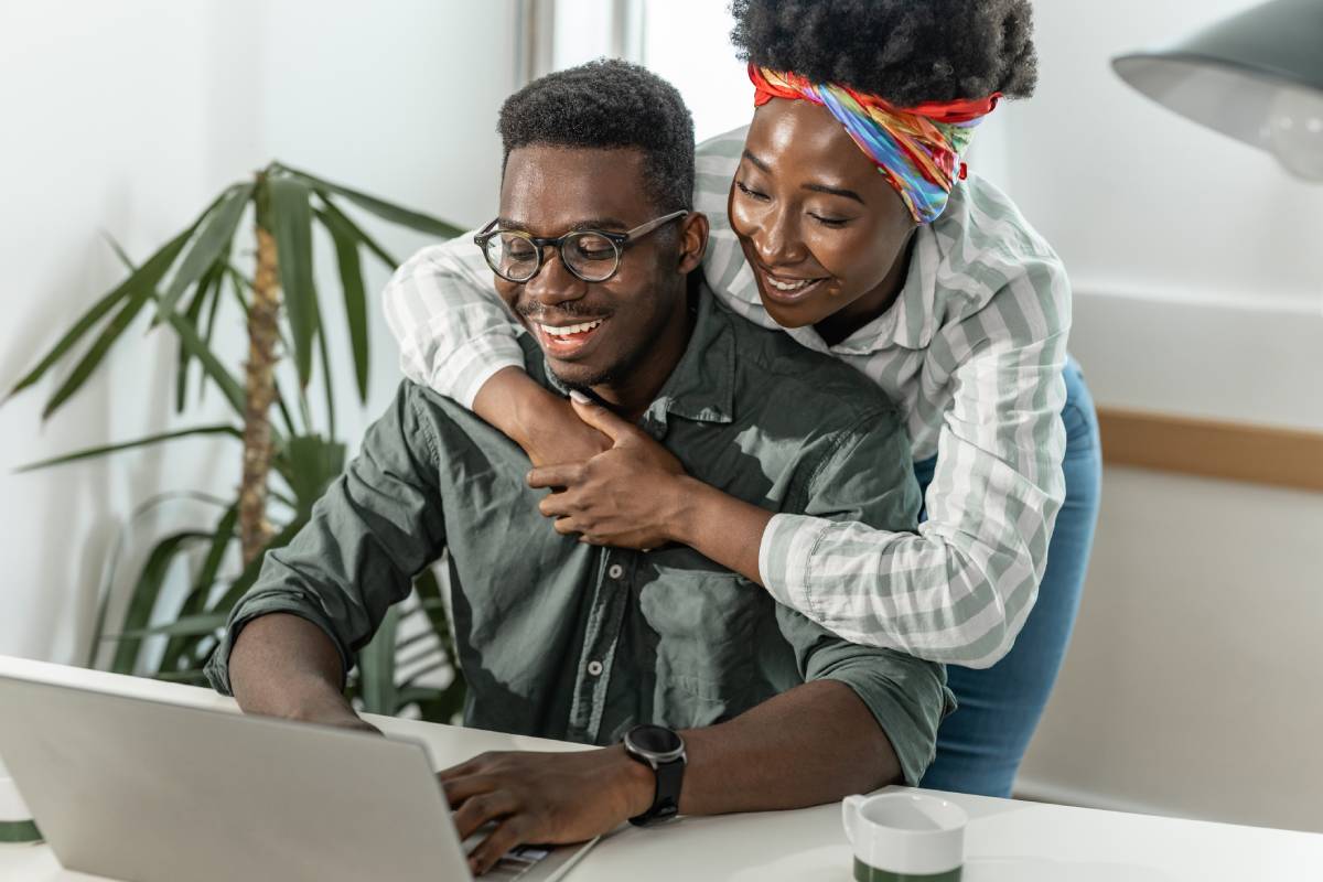 Smiling couple looking at information on a laptop screen.