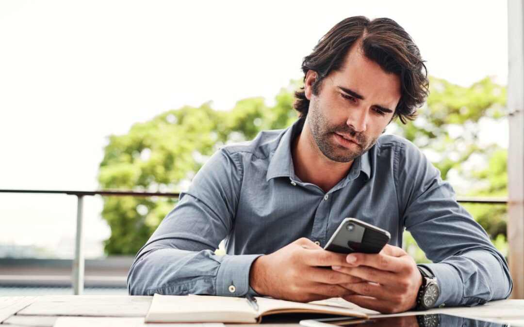 Man replying to a phone text while sitting at a work table