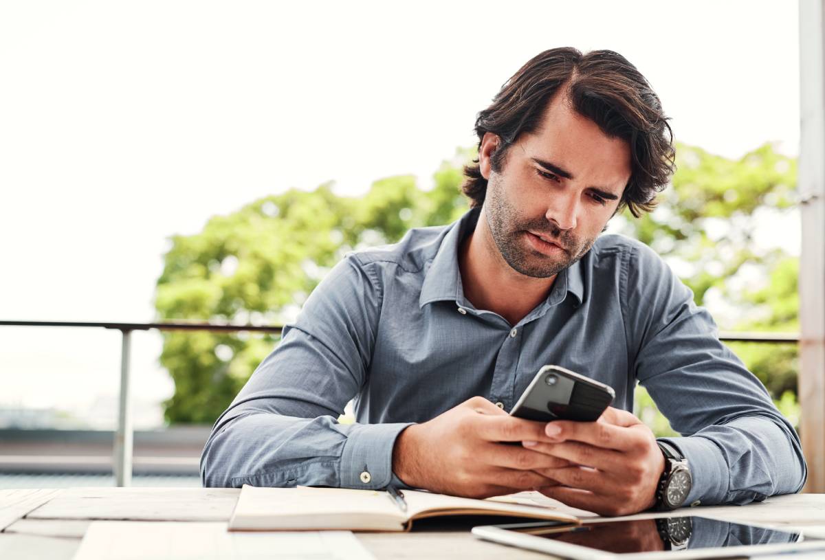 Man replying to a phone text while sitting at a work table