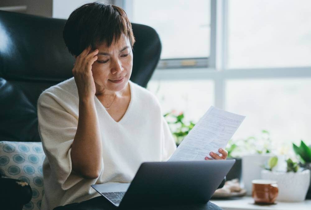 Woman worried about tax identity theft as she looks at her laptop and a tax document in her living room.