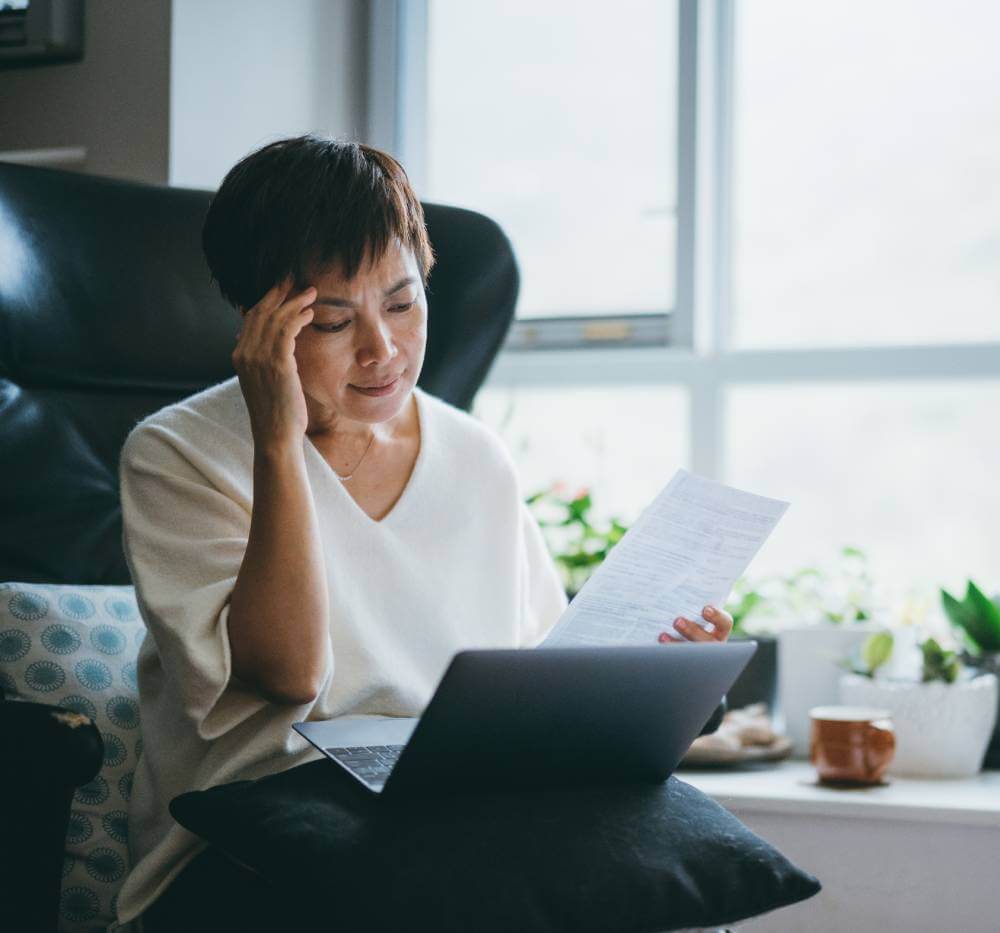 Woman worried about tax identity theft as she looks at her laptop and a tax document in her living room.