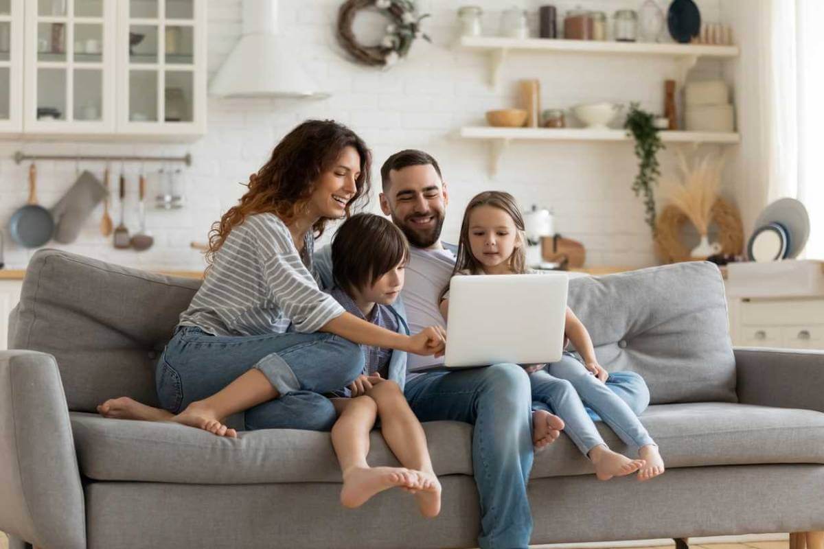 Mother, father, young boy and young girl, sitting on a sofa and preventing child identity theft using their laptop.