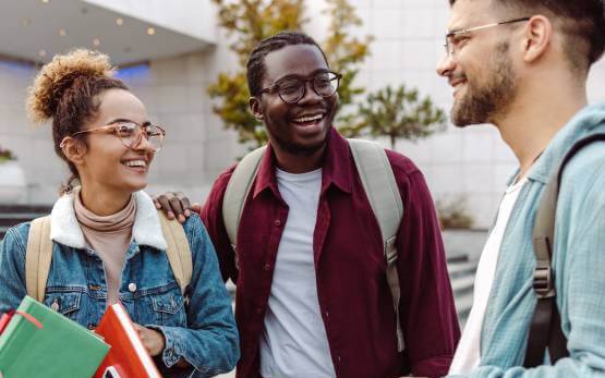 A group of 3 college students talking in front of a campus building.