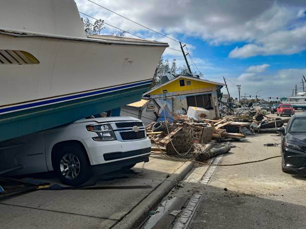 Hurricane damage after a natural disaster with boat on top of vehicle and scattered storm debris.