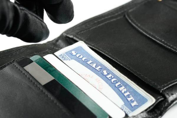 Thief stealing a Social Security card in a man's wallet.